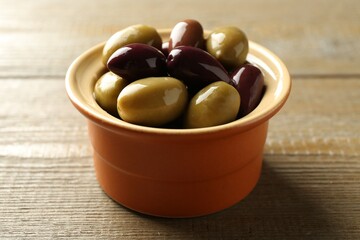 Tasty olives in bowl on wooden table, closeup