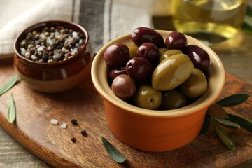 Tasty olives in bowl, leaves and spices on wooden table, closeup