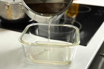 Pouring Used cooking oil into glass container at white countertop, closeup