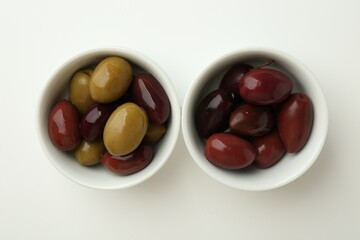 Tasty marinated olives in bowls on white table, flat lay