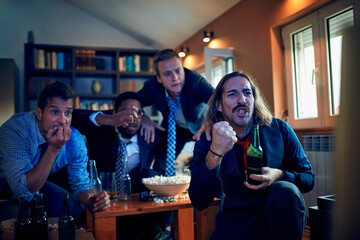 Young group of men watching a football game after work in a living room on the tv