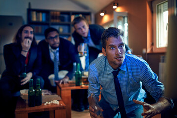 Young group of men watching a football game after work in a living room on the tv