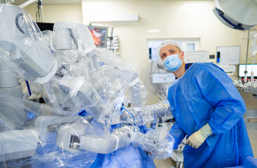 Surgeon using robot arm in OR. A surgeon in blue scrubs uses a robotic arm during a surgical...