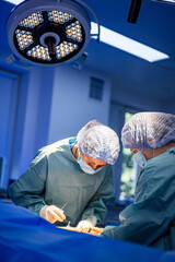Surgeons operate in hospital. Two surgeons are focused on an operation under bright lights in a...