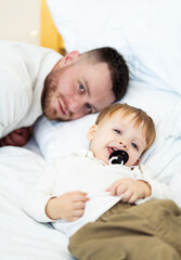 Father and son relaxing on the bed. A father lies on a bed next to his young son, who is playfully...