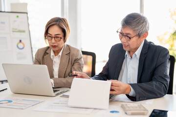Man and woman are working on a presentation in meetimg room modern office. hand holding a clipboard with graphs and typing on a laptop.