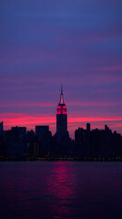 Obraz premium New York skyline at dusk, the city lights reflecting on the water with a colorful sky in the background 