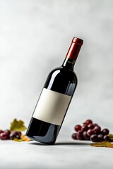 Obraz premium tilted bottle of red wine, front view, full body photo, minimalistic grey background with red grapes and green leaves