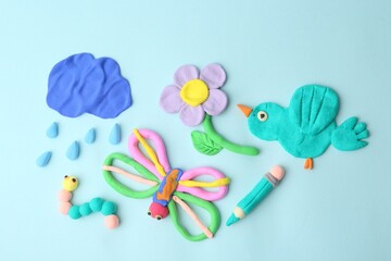 Different colorful child's crafts made of play dough on light blue background, flat lay