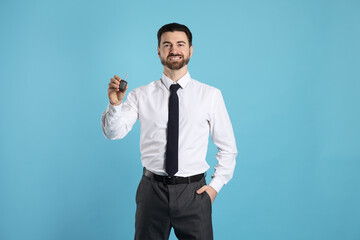Cheerful salesman with car key on light blue background