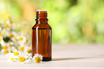 Bottle of essential oil and chamomile flowers on white wooden table against blurred background, closeup. Space for text