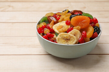 Mix of different dried fruits in bowl on wooden table, closeup. Space for text