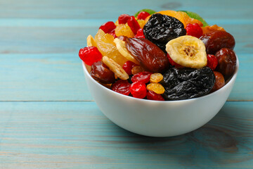 Mix of different dried fruits in bowl on blue wooden table, closeup