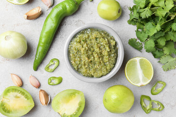 Delicious salsa sauce in bowl and ingredients on light textured table, flat lay