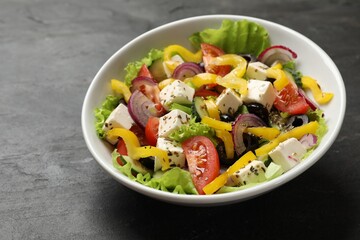 Delicious fresh Greek salad in bowl on black table, closeup