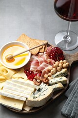 Different types of cut cheese and other snacks served with wine on gray table, closeup