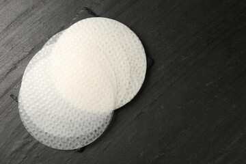 Edible rice paper sheets on dark textured table, top view. Space for text