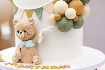 A beautifully crafted teddy bear fondant decoration on a first birthday cake, featuring pastel...