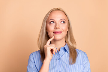Charming professional woman with blue striped shirt making a thoughtful gesture and smiling against a beige background