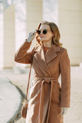 Woman in a beige coat wearing sunglasses on a sunny day