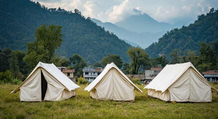 A group of white canvas tents stands in a grassy area, framed by mountains and a peaceful environment under a partly cloudy sky
