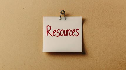 A sticky note with the word "Resources" written in red, clipped to a beige background, symbolizing organization and information management.