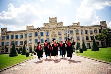 Joyful group of students celebrating graduation outdoors on a sunny day in front of a historic...
