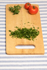 tabla de cortar de madera con perejil picado, al fondo una rama de perejil y un par de tomates