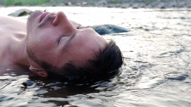 Primer plano de un hombre flotando en un r&iacute;o con los ojos cerrados. Su expresi&oacute;n refleja tranquilidad y relajaci&oacute;n. El agua fluye suavemente a su alrededor, creando un ambiente sereno y natural.