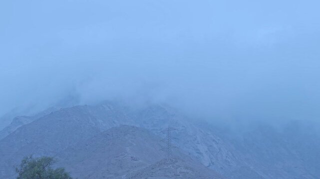 Paisaje monta&ntilde;oso cubierto por neblina con tonos fr&iacute;os y ambiente brumoso. Se observa una torre de alta tensi&oacute;n en la ladera, destacando la conexi&oacute;n entre la naturaleza y la infraestructura humana.