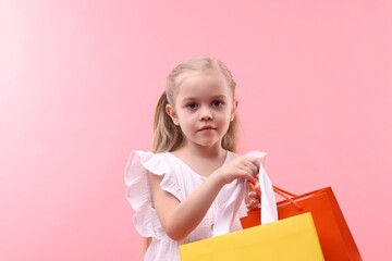 Fototapeta premium Little girl with shopping bags on pink background
