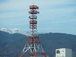 Red and white telecommunications tower with snowy mountains in the background in Japan