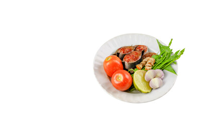 A white plate holds catfish slices, tomatoes, turmeric, and water spinach, ready for a traditional dish preparation.