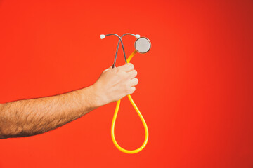 Doctor holding a yellow stethoscope against a vibrant red background, symbolizing healthcare and medical examination. Highlighting auscultation for accurate diagnosis and patient care
