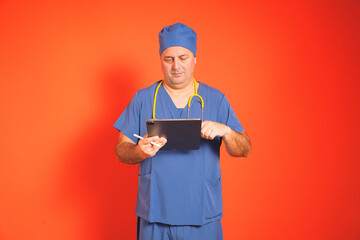Surgeon wearing blue scrubs and yellow stethoscope using digital tablet and stylus pen, working on...