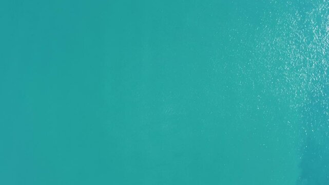 The camera spins as it falls towards the sea. Sea surface, aerial drone video. Waves on the sea. Turquoise sea.