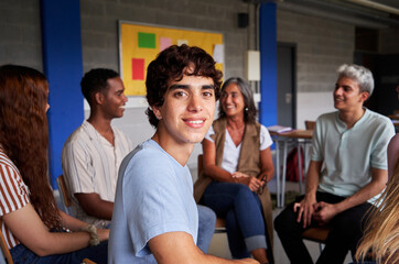 Obraz premium Portrait of a brunette young man sitting in circle next to his school friends during a class, looking at the camera smiling. Copy space image.