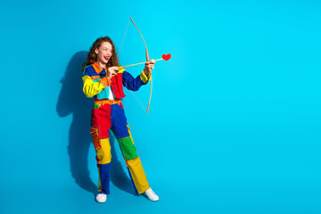 Cheerful young woman in vibrant outfit posing with a heart on an arrow against a blue background
