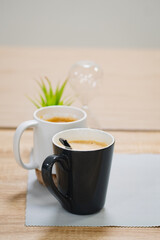 Side view of hot latte coffee  in a white cup and black cup on wooden table