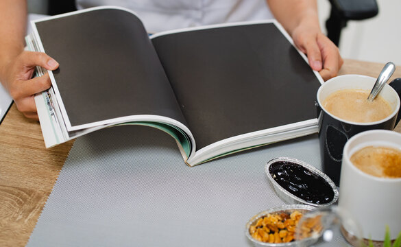 Top of hand holding glass of hot milk and opening  blank magazine with coffee  on wooden table in muck up and flat lay concept	
