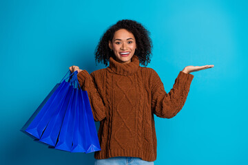 Joyful young woman holding shopping bags in front of a blue background