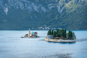 Bay of Kotor, Montenegro - July 2, 2024: Perast islands. Sveti Juray hotels and its private park on one. Church of Our Lady of Skrpjela on the smaller one. Forested coastline in back