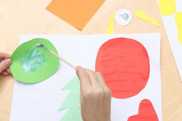 Girl applying glue onto paper figure for her creative project at table indoors, above view. Art and...