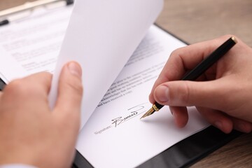 Man putting signature on document at table, closeup
