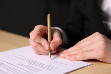 Woman putting signature on document at table, closeup