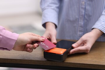 Woman paying with credit card via terminal at wooden counter indoors, closeup