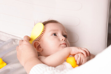 Woman brushing hair of her little baby indoors, closeup