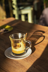 Glass cup with hot golden turmeric latte on wooden table in sunlight. Warm autumn mood, cozy coffee shop atmosphere