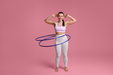 Smiling woman training with hula hoops on pink background