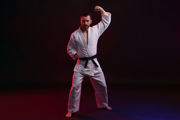 Man wearing uniform practicing karate in color lights against black background